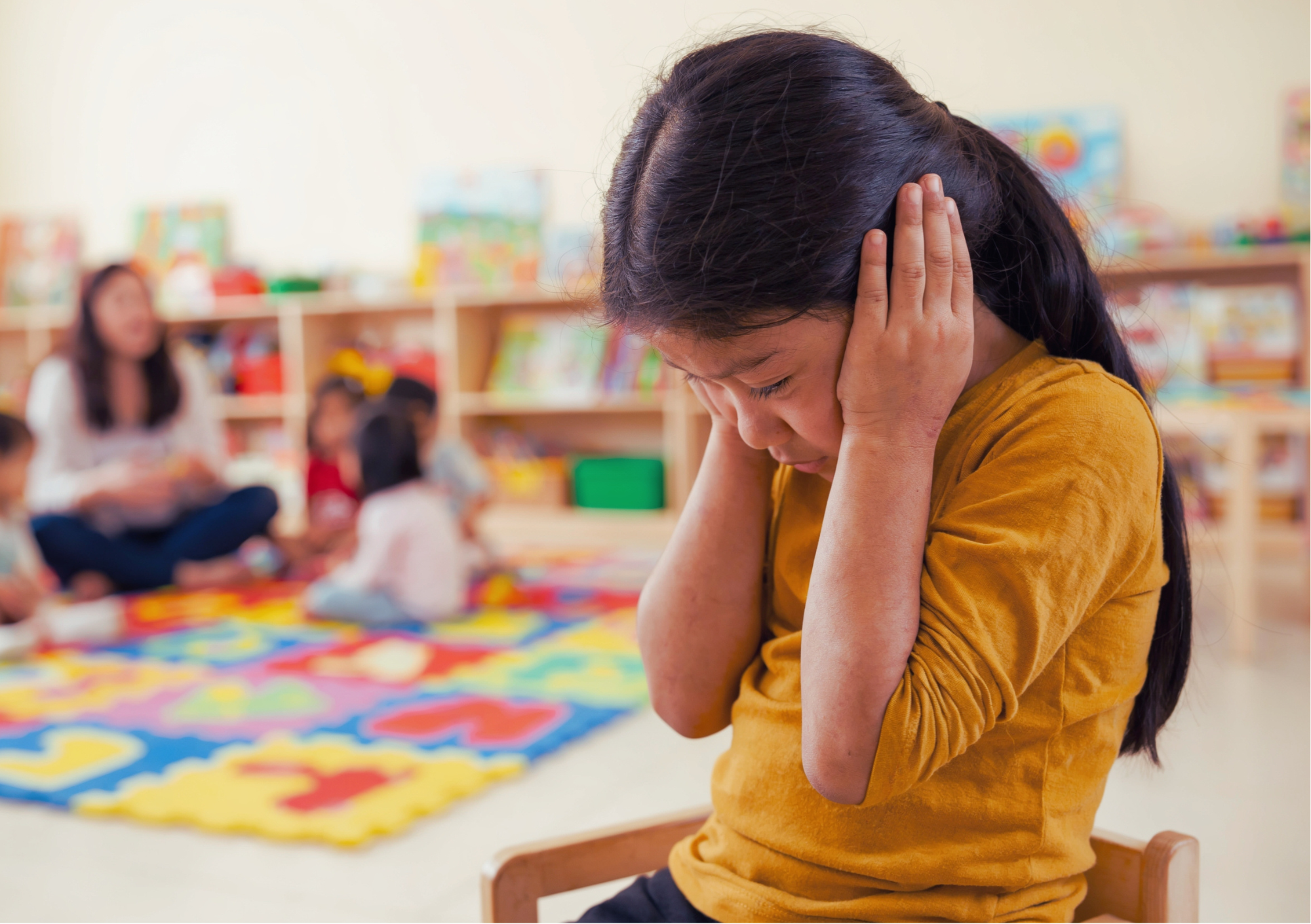 Young girl covering her ears in a classroom showing signs of anxiety